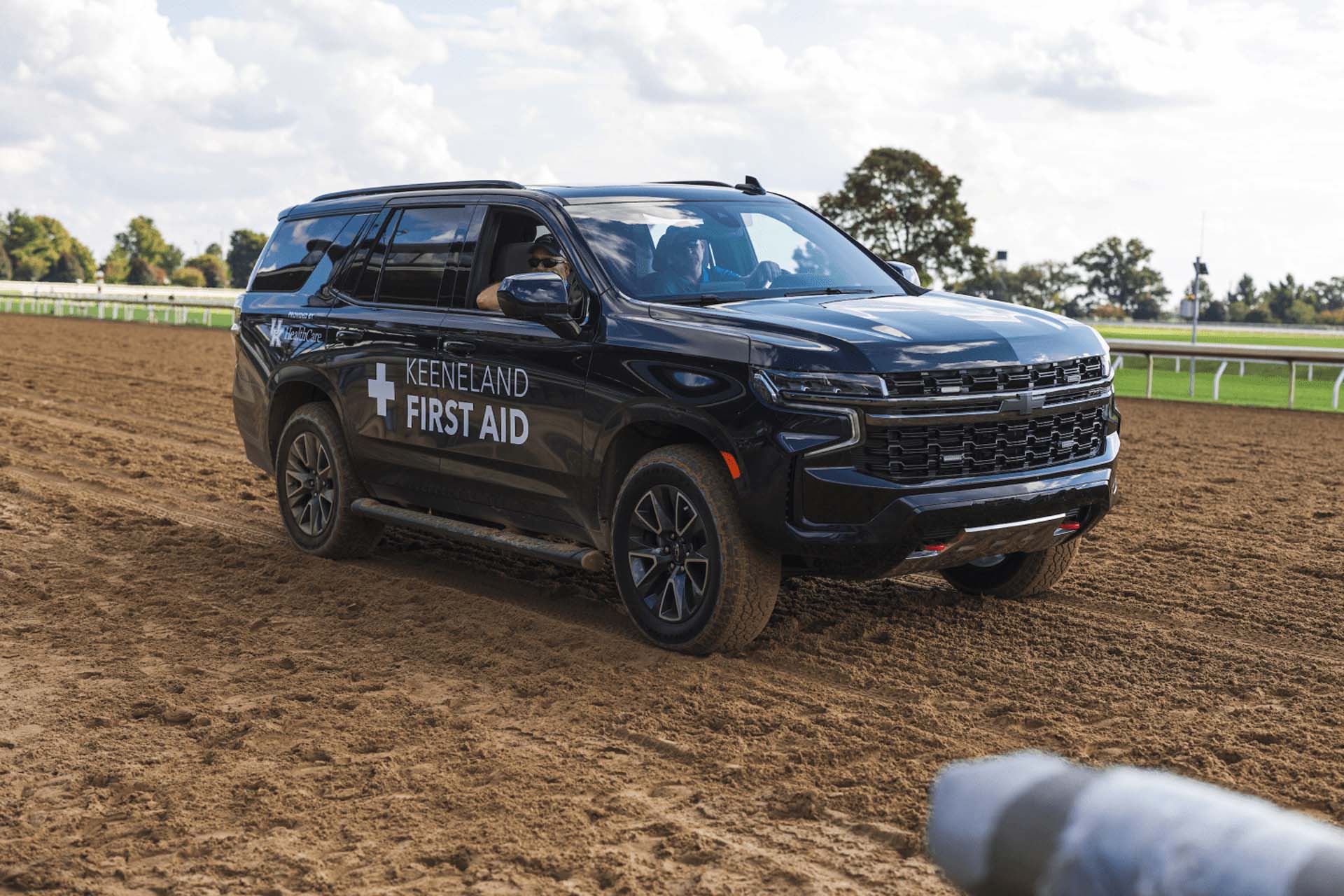 A picture of the Keenlandsscape First Aid car on the dirt track. It is a large black Chevy SUV.